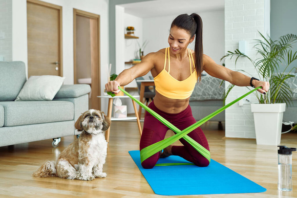 Young muscular build woman using resistance band while working out in the living room. - Fotó, kép