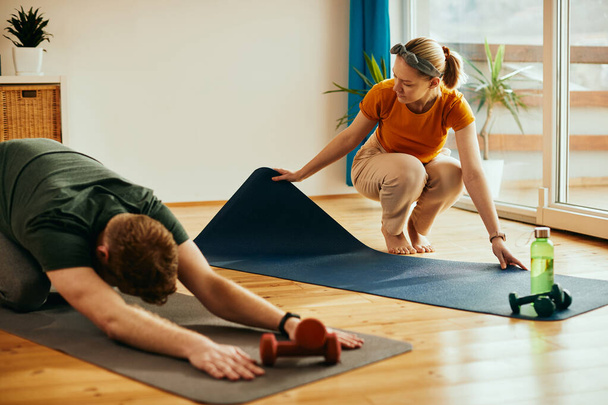 Athletic couple exercising together at home. Focus is on woman preparing her exercise mat. - Фото, зображення