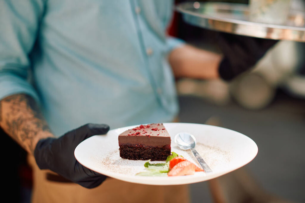 Close-up of waiter wearing protective gloves while serving dessert in a cafe. - 写真・画像