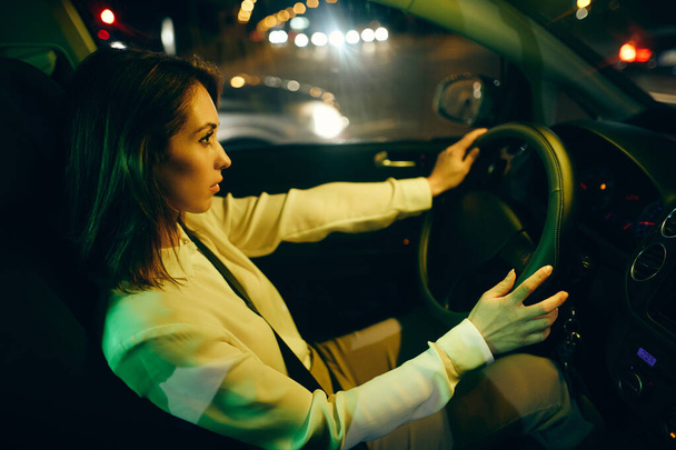 Profile view of a young woman driving car at night.  - 写真・画像