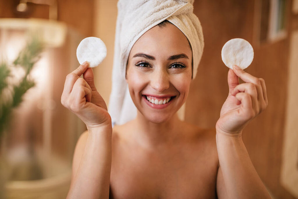 beautiful happy woman holding two cotton pads while looking at camera in the bathroom.  - Foto, imagen