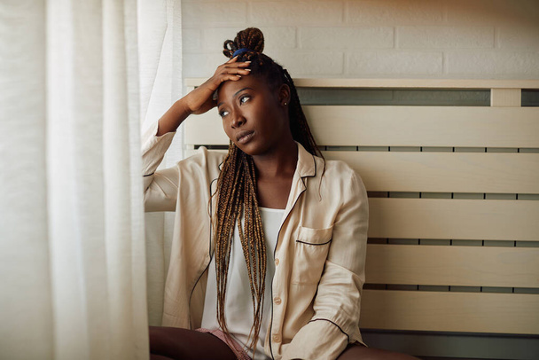 Depressed black woman looking through the window and thinking of something at home. Copy space. - Fotó, kép