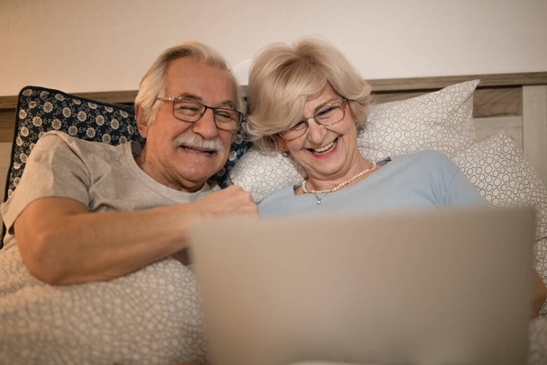 Happy mature couple having fun while surfing the net on laptop in bedroom at night.  - Photo, image