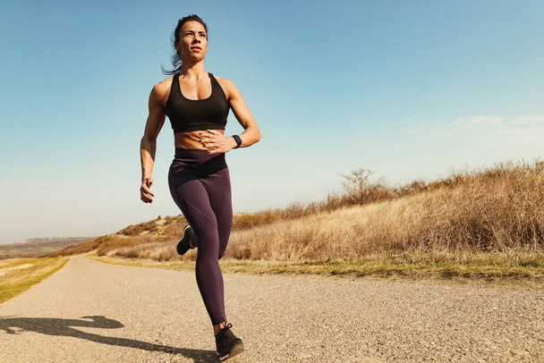 Low angle view of determined muscular build woman jogging on the road. Copy space. - Fotografie, Obrázek