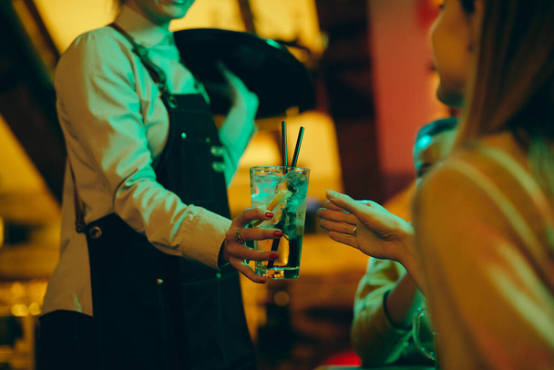 Close-up of waitress serving drinks to guests in a pub at night. - Foto, afbeelding