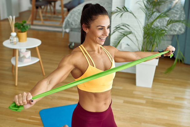 Happy muscular build woman exercising with resistance band at home.  - Fotografie, Obrázek