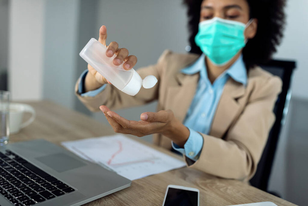 Close-up of African American businesswoman using hand sanitizer while working in the office during coronavirus pandemic.  - Foto, afbeelding