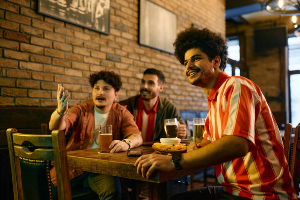 Happy Lebanese man and his male friends watching sports game on TV in a bar.  - Foto, Imagem