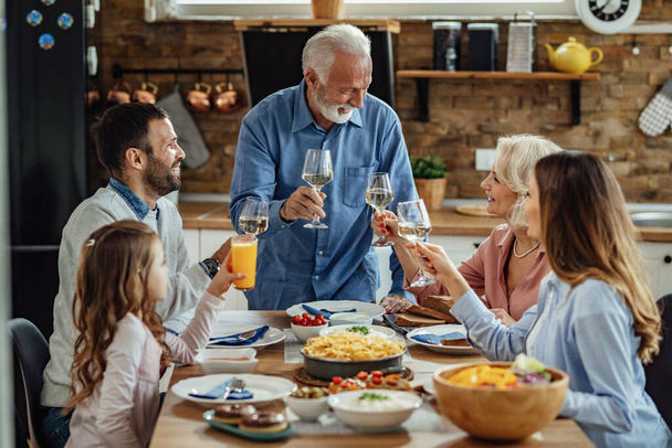 Happy multi-generation family toasting while having lunch together at dining table.  - Foto, Bild