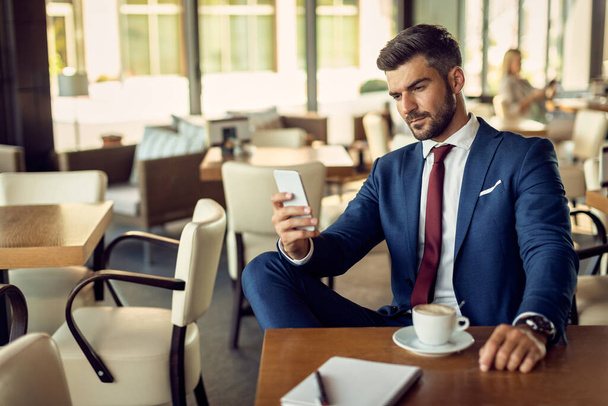 Удумливий бізнесмен смс на мобільному телефоні, маючи чашку кави в кафе
.  - Фото, зображення