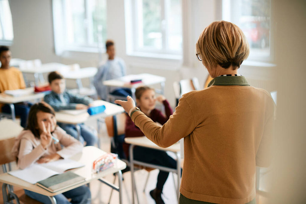 Rear view of elementary school teacher pointing at one of her students who is raising arm to answer a question. - Photo, image