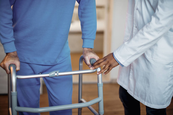 Unrecognizable doctor assisting senior man with mobility walker during physical therapy at nursing home.  - Photo, Image