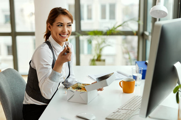 Young happy businesswoman using computer while having lunch break in the office.  - Photo, image