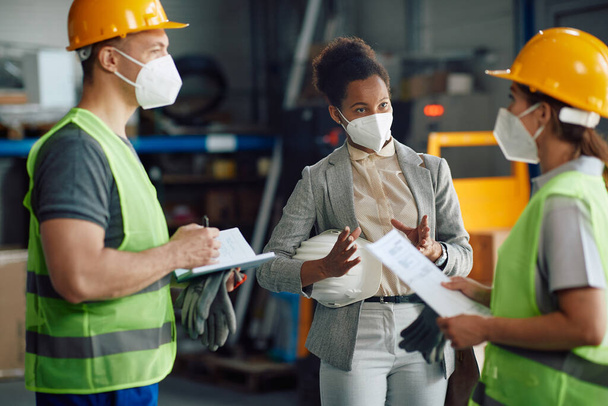 Black female supervisor and workers talking at distribution warehouse while wearing protective face masks. - Foto, Imagem
