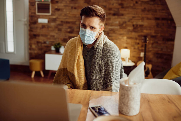 Man with face mask feeling unwell and calling his doctor via video call from home. - Foto, Imagen