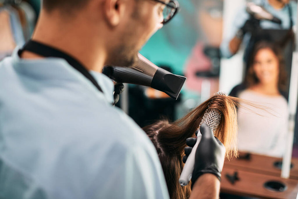 Close-up of hairstylist using blow dryer and round brush while styling customer's hair at the salon. - Fotoğraf, Görsel