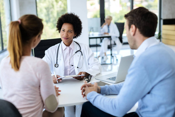 Черная женщина-врач разговаривает с парой во время медицинской консультации в больнице.  - Фото, изображение