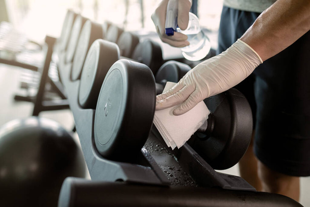 Close-up of athlete wearing protective gloves and disinfecting hand weights at health club.  - Foto, imagen