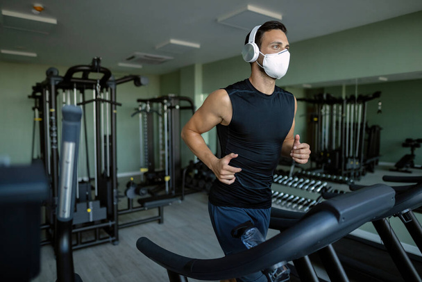 Athletic man wearing face mask while running on running track in health club during coronavirus epidemic.  - Zdjęcie, obraz