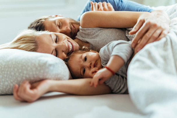Щасливі батьки і їх маленька дочка відпочивають на ліжку
.  - Фото, зображення