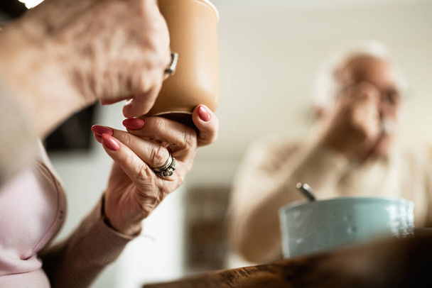 Close-up van volwassen vrouw met een kopje koffie tijdens het ontbijt met haar man thuis.  - Foto, afbeelding