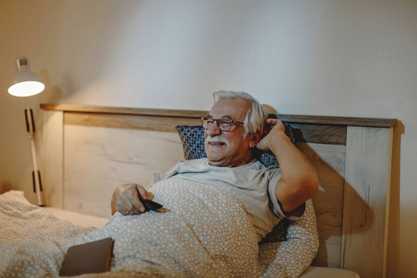 Happy mature man enjoying while watching TV in bed at night.  - Foto, afbeelding