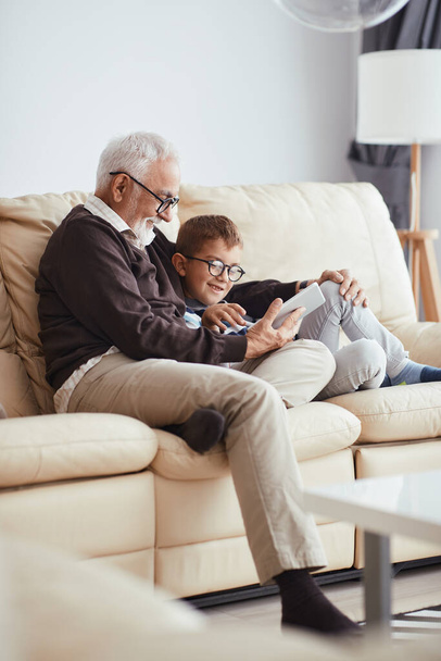 Happy little boy enjoying with hi grandfather while using touchpad together at home. - Φωτογραφία, εικόνα
