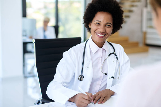Portrait of happy black doctor working at her office and looking at camera.  - Foto, Imagem