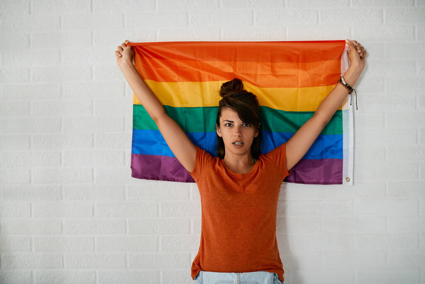 Young woman with raised arms holding LGBT flag and looking at camera.  - Foto, immagini