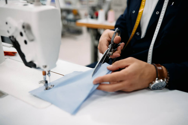Close-up of tailor using scissors while working with sewing machine at textile factory. - 写真・画像