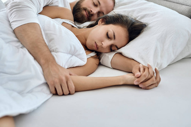 Молода ласкава пара тримає руки під час сну в спальні
.  - Фото, зображення