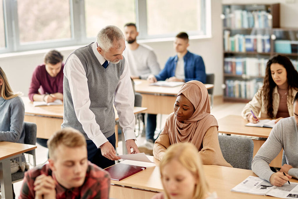 Зрілий вчитель спілкується з чорношкірим ісламським студентом, допомагаючи їй в університетському класі.. - Фото, зображення