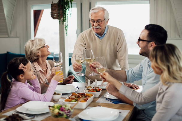 Happy multi-generation family toasting while having lunch together at dining table. Focus is on senior man. - Foto, Imagen
