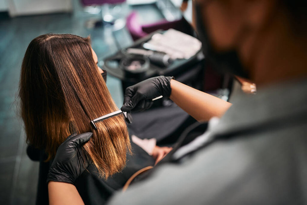 Крупним планом перукар використовує гребінець під час чищення волосся клієнта в перукарні
. - Фото, зображення
