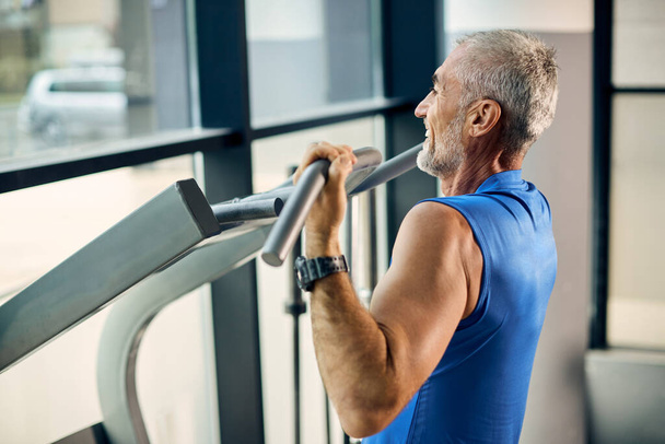Happy mature athlete practicing pull-ups while working out at health club.  - Foto, Imagem
