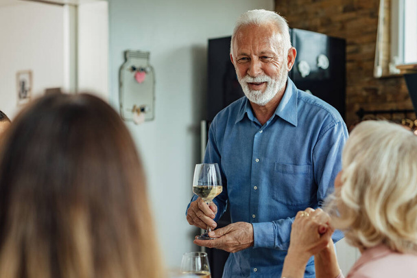 Happy senior man holding glass of wine and communicating with his family in dining room. - Fotoğraf, Görsel