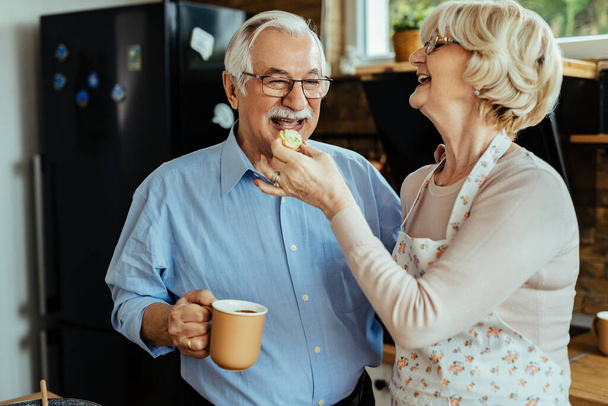 Happy mature man having fun with his wife while she is feeding him in the kitchen.  - Zdjęcie, obraz