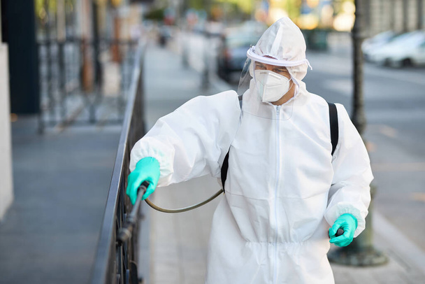 Працівник з дезінфекції в костюмі з розпиленням вулиць міста під час пандемії COVID-19
.  - Фото, зображення