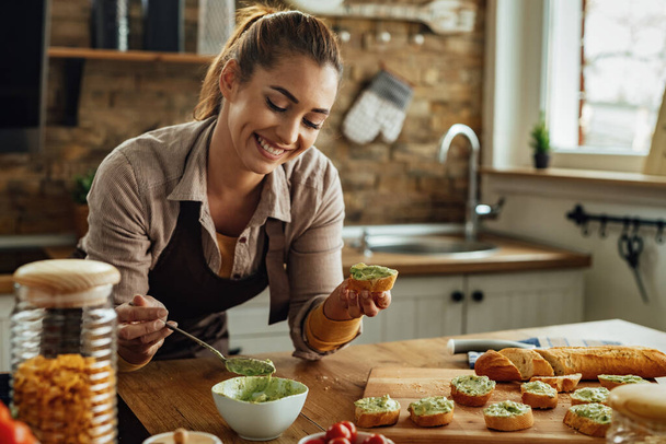 Młoda uśmiechnięta kobieta robi awokado bruschetta w kuchni.  - Zdjęcie, obraz