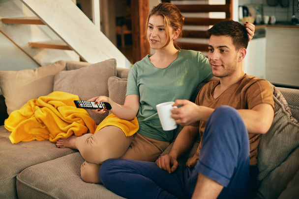 Smiling woman changing channels while watching TV with her boyfriend at home.  - Zdjęcie, obraz