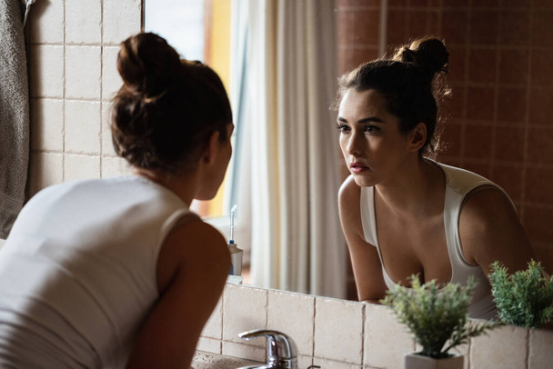 Pensive woman looking herself in the mirror in bathroom. - Foto, immagini