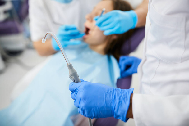 Close-up of orthodontist using dental aspirator for saliva during teeth examination of a patient at dental clinic.  - Photo, image