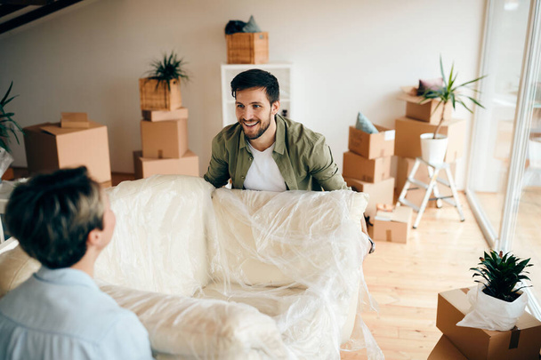 счастливый мужчина и его жена несут диван в гостиной своего нового дома.  - Фото, изображение