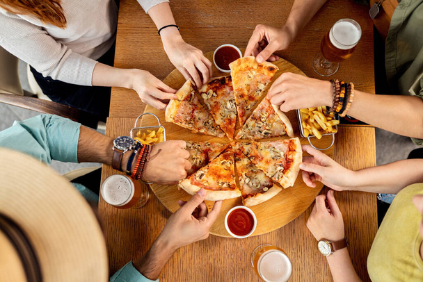 Високий кут зору групи друзів, які мають піцу на обід у пабі
.  - Фото, зображення