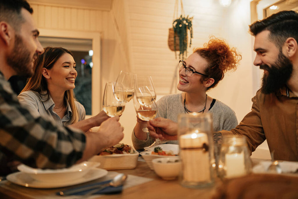 Small group of happy friends having fun while toasting during dinner at home. Focus is on redhead woman.  - Photo, image
