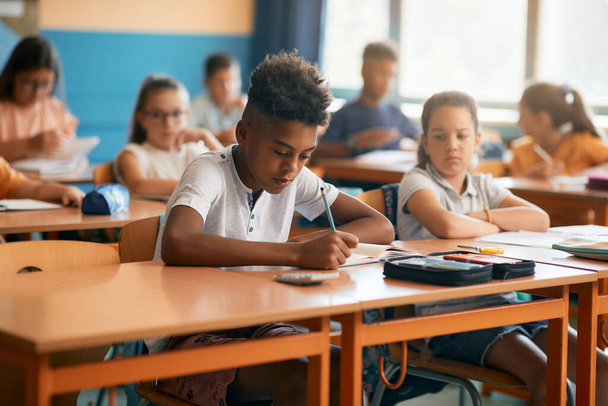 Афроамериканський школяр пише під час уроків з однокласниками в початковій школі.. - Фото, зображення