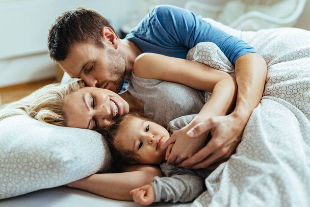 Young happy family enjoying in their morning while lying down on bed together.  - Photo, Image