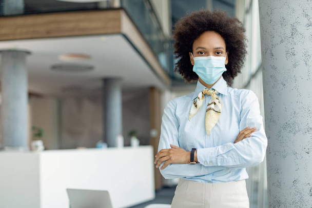 Successful black businesswoman wearing face mask while standing with arms crossed  in the office.  - Fotografie, Obrázek