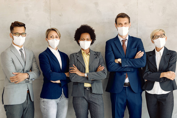 Group of happy business people standing with crossed arms and wearing protective face masks while looking at camera.  - Fotó, kép
