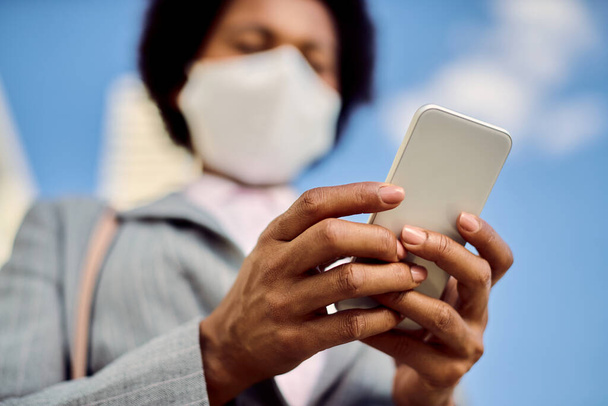 Close-up of black businesswoman with protective face mask using mobile phone outdoors. - Photo, image